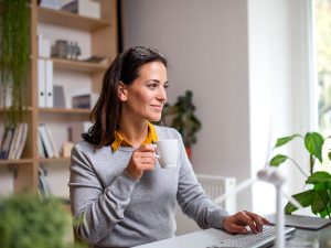 donna davanti al computer che beve una tazza di caffè